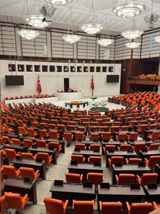 Interior view of the Turkish Grand National Assembly in Ankara, featuring orange seats and a modern design. Paradise Collapse governance chamber interior