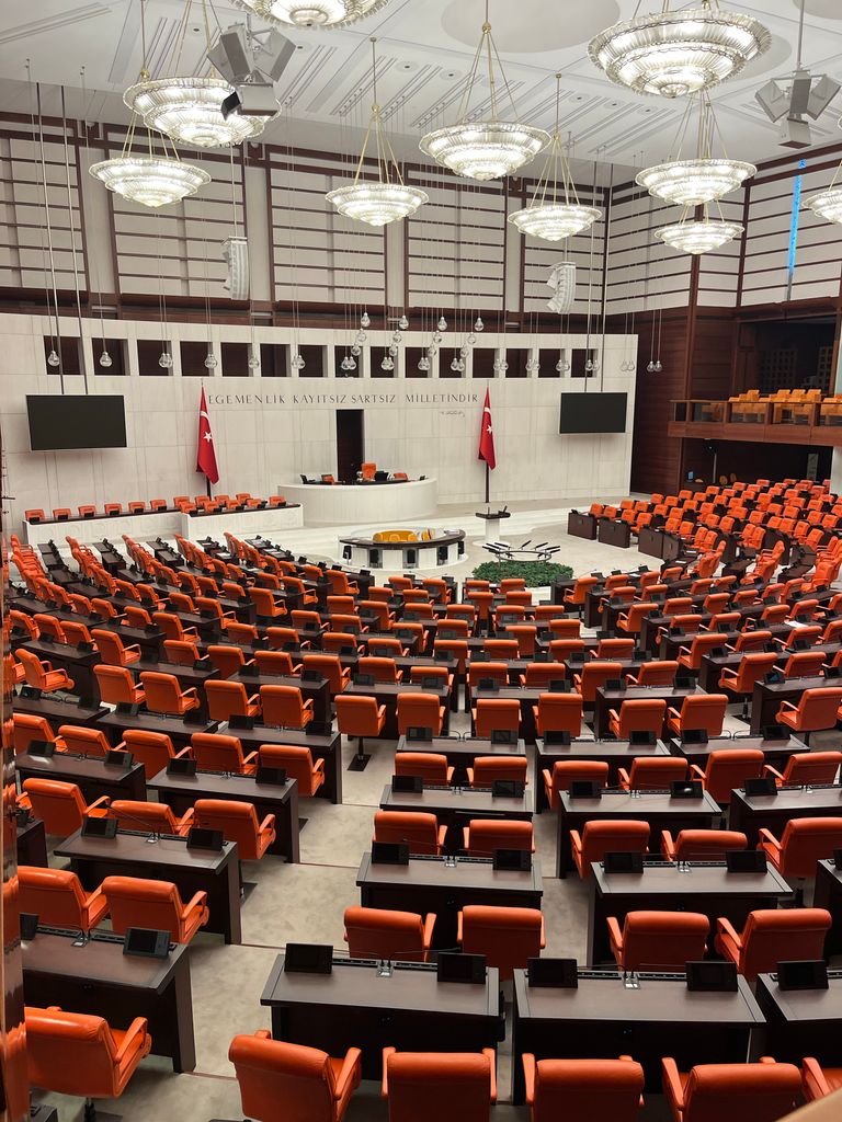Interior view of the Turkish Grand National Assembly in Ankara, featuring orange seats and a modern design. Paradise Collapse governance model illustration